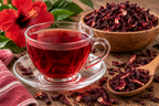 Infuzie de hibiscus roșu-rubiniu într-o ceașcă de sticlă, lângă un bol cu flori uscate